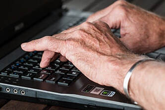aged hands typing on computer